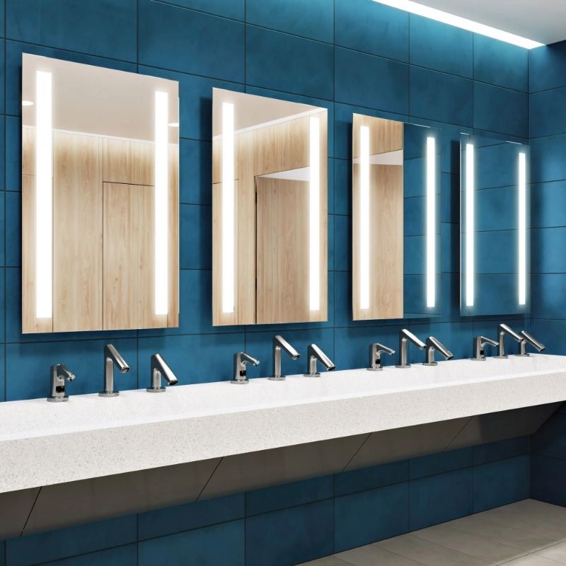 Lavatory area featuring Sloan backlit mirrors and automatic chrome faucets mounted on a white countertop, set against a deep blue tiled wall.