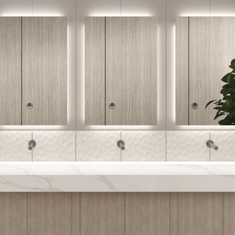 Modern sinks with recessed Sloan faucets and backlit mirrors in light wood finish, set above a white marble countertop.