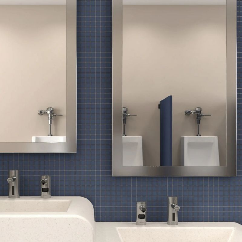 Sinks with Sloan automatic faucets in front of metal-framed mirrors, in a restroom with blue tiles and urinals reflected in the background.