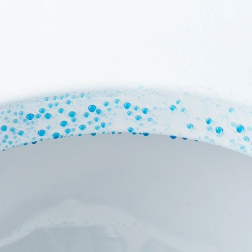 Close-up of blue water droplets on the inner surface of a Sloan toilet, representing cleanliness and freshness.