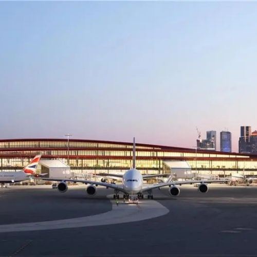 Airplane on the runway in front of a modern airport terminal with a glass facade at sunset.