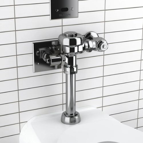 Exposed Sloan flushometer in polished chrome finish installed above a toilet against a beige veined marble wall with a recessed sensor plate.