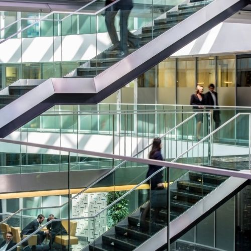 Modern office interior with people walking on glass staircases in an open, multi-level space.