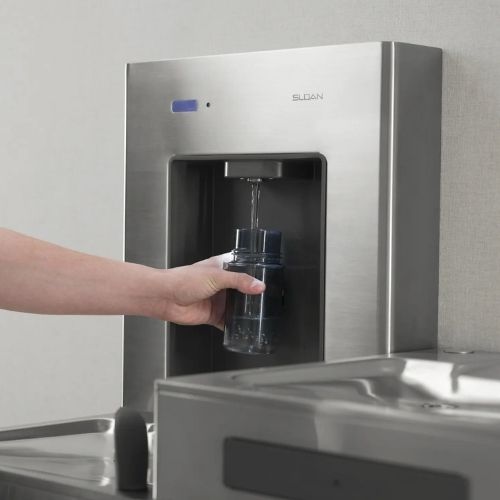 Hand refilling a reusable bottle at a stainless steel Sloan water dispenser.