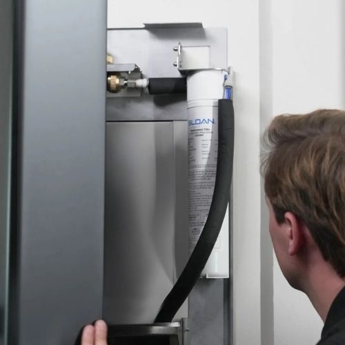 Technician inspecting the water filtration system inside a Sloan bottle filler.