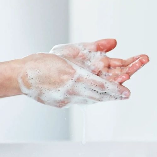 Hands covered in soap under water showing the handwashing process.