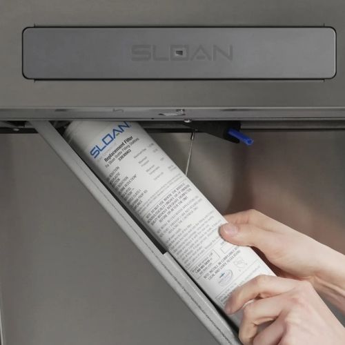 Close-up of hands replacing a Sloan water filter cartridge inside a dispenser.