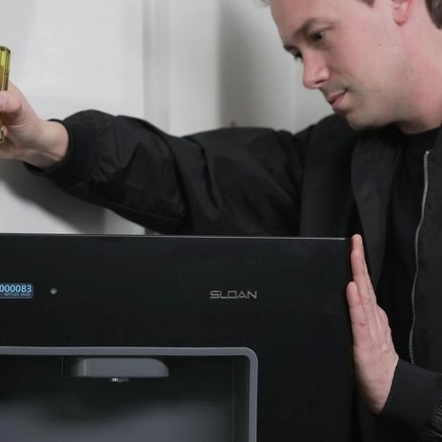 Technician installing a black Sloan bottle filler on a wall, using a level to ensure proper alignment.