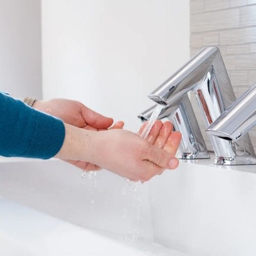 Hands washing under Sloan chrome touchless faucets