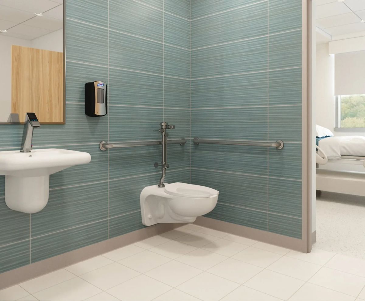 Baño accesible con lavabo mural, dispensador de jabón, barras de apoyo y sanitario suspendido; se observa una habitación de hospital al fondo.