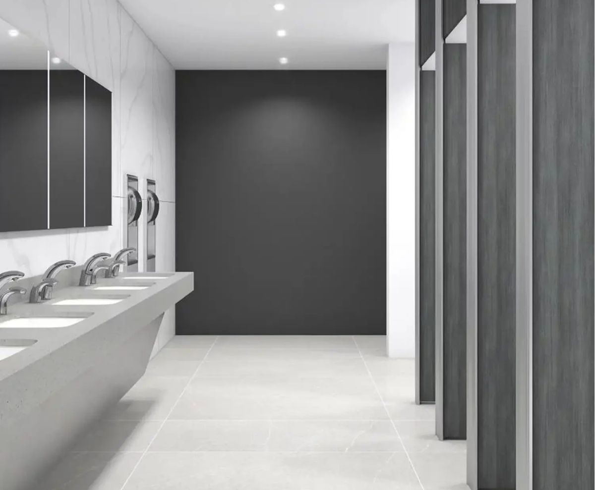 Contemporary restroom with aligned solid-surface sinks, automatic faucets, and private stalls featuring gray and white finishes.