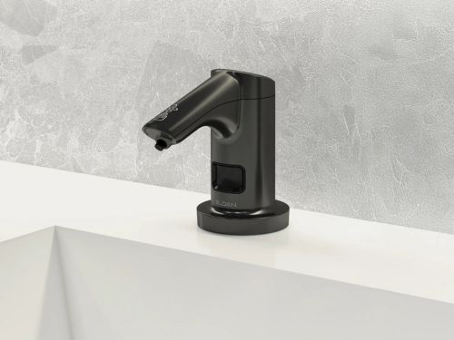 Dispensador automático de jabón en acabado negro mate sobre un lavabo blanco, con un fondo de pared texturizada.