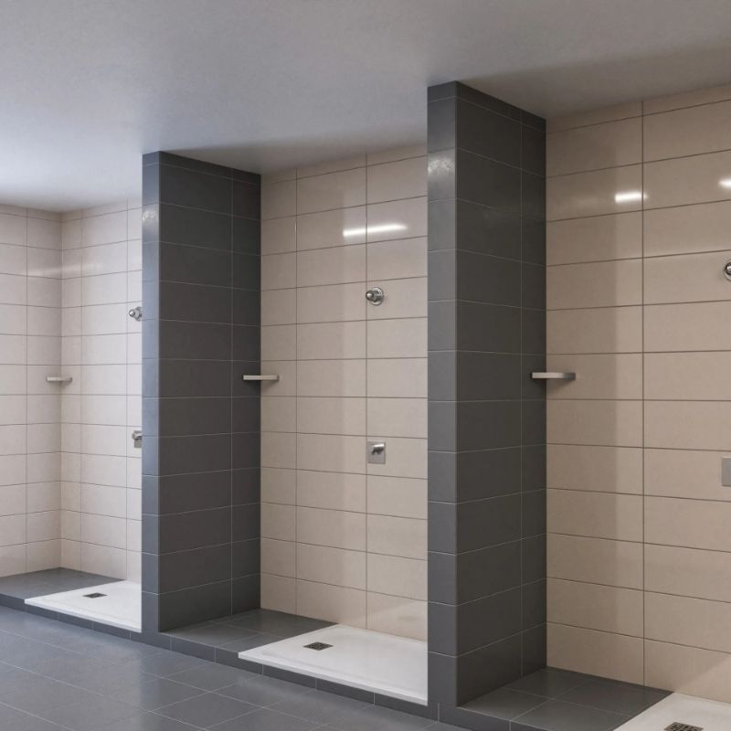Commercial shower area with gray and beige tiled walls, featuring Sloan Act-O-Matic® showerheads and individual partitions.