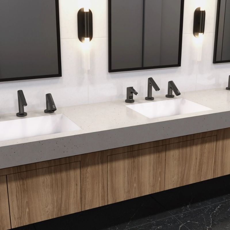 Lavabos empotrados con grifos automáticos en acabado negro mate, sobre una encimera de superficie sólida gris claro y un mueble de madera natural.