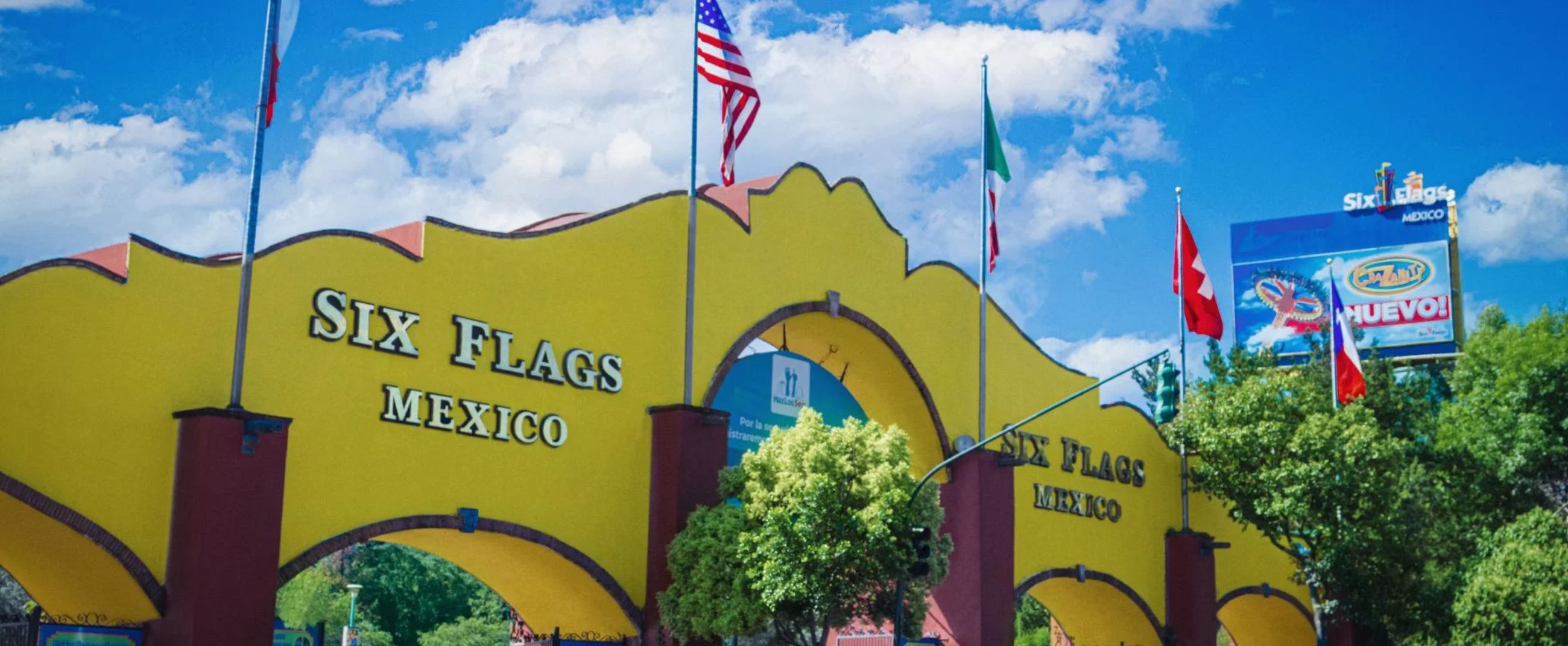 Main entrance of Six Flags Mexico featuring its iconic yellow arch, surrounded by international flags under a bright, inviting sky.