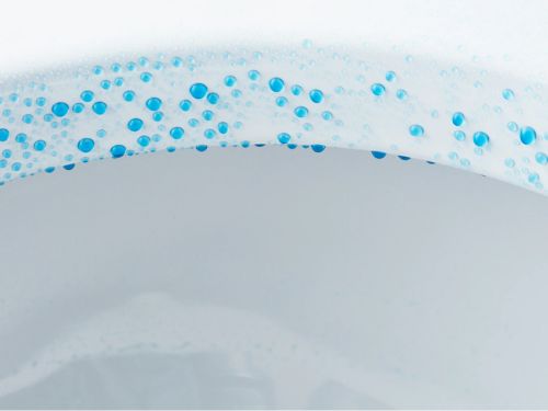 Primer plano del interior de una taza de baño con gotas de agua azul que resaltan una superficie esmaltada suave y limpia.