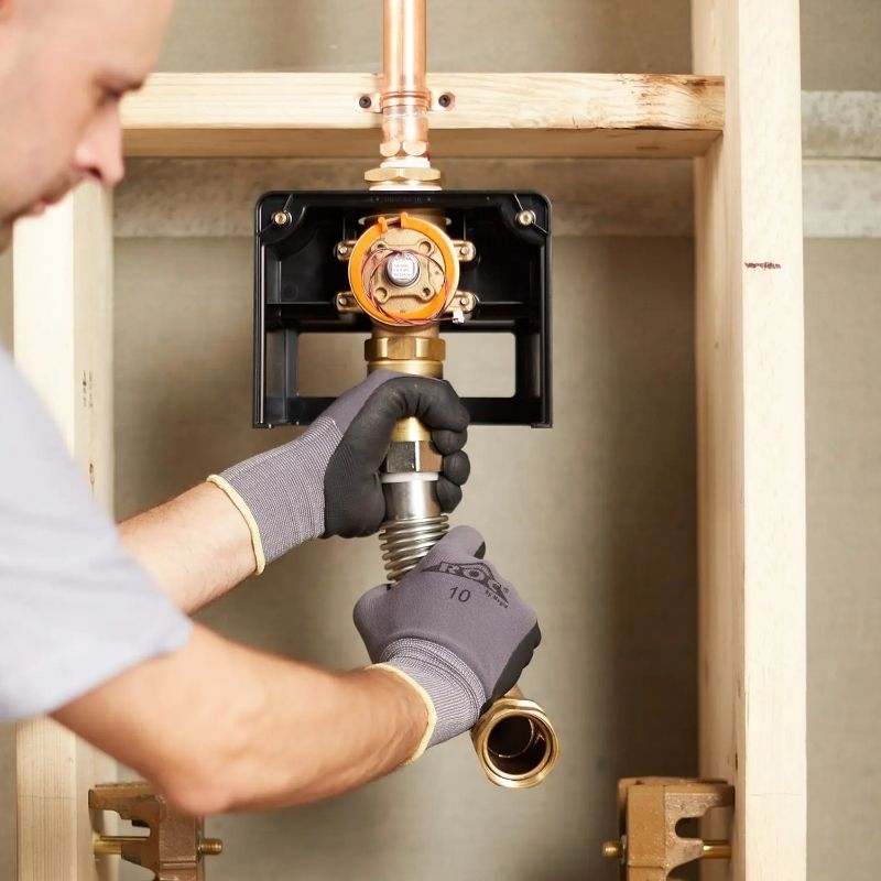 Plumber installing Sloan flushometer behind wall frame