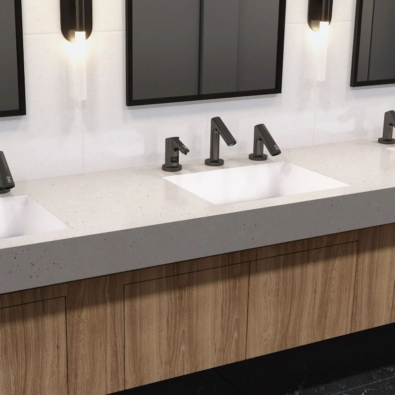Modern sink with Sloan faucets in a matte black finish installed on a light stone countertop.