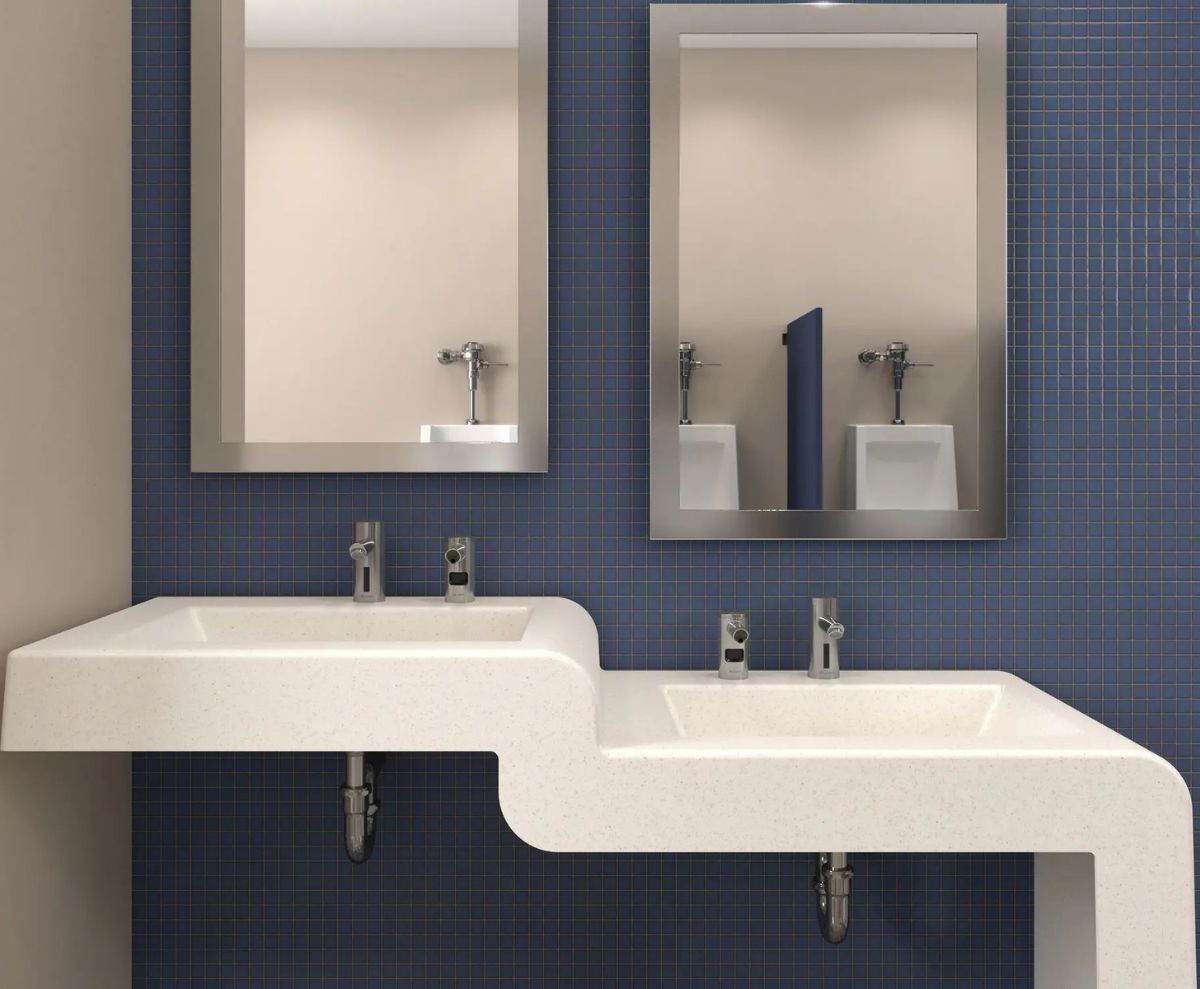 Lavabos de superficie sólida con diseño tipo cascada y grifos automáticos, instalados debajo de espejos rectangulares sobre un muro de mosaico azul.