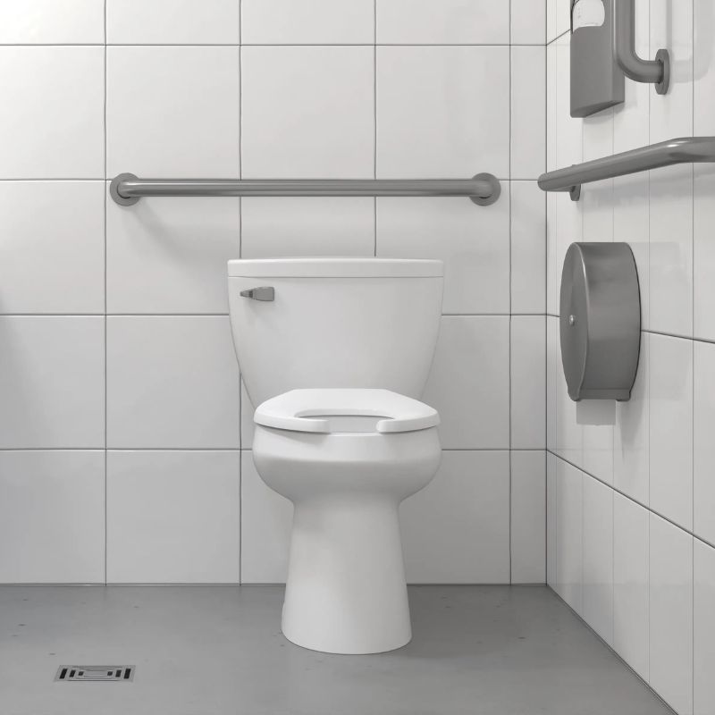 Toilet with tank installed in an accessible restroom featuring stainless steel grab bars and white tiled walls.