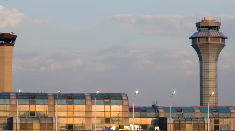 modern airport terminal at sunset, with two control towers visible in the background. The main structure features a curved design with reflective glass that captures the golden tones of the setting sun. The walkways and windows shimmer with warm light, while the towers—one taller and slimmer, the other more robust—stand out against the sky, symbolizing the airport’s operational core.