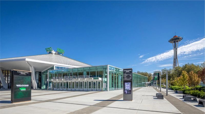 Main facade of Climate Pledge Arena in Seattle, featuring modern glass architecture with the iconic Space Needle in the background under a clear sky.