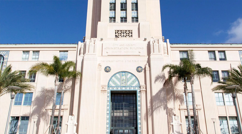 the City and County Administration Building in San Diego, California, an iconic Art Deco structure inaugurated in 1938. Its design features elegant vertical lines, blue ceramic details, and a grand main entrance symbolizing civic authority and public service. The façade bears the inscription “The Noblest Motive is the Public Good,” reflecting its role as an administrative center devoted to serving the community.