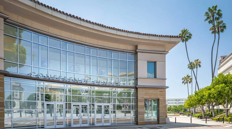 Pasadena Convention Center in California, featuring a modern design with large glass windows and a metal framework that allows abundant natural light. The building’s curved lines, light stone panels, and neutral tones blend seamlessly with the urban surroundings. In front, a brick-paved plaza and tall palm trees frame the main entrance, conveying a bright, orderly atmosphere characteristic of contemporary Californian architecture.