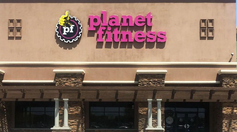 Exterior facade of a Planet Fitness gym featuring its iconic purple and yellow logo, symbolizing wellness and positive energy.