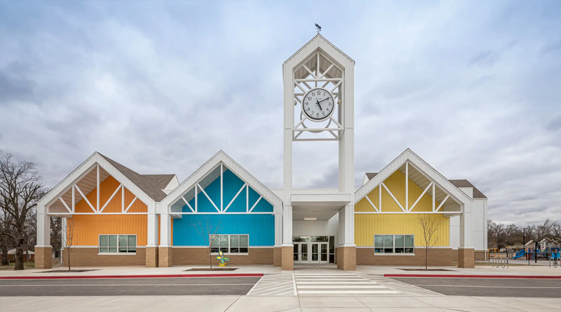 main façade of Westwood Elementary, a contemporary school building that blends clean geometric forms with a vibrant color palette (yellow, blue, and orange). The central clock tower adds a classic yet functional touch, while the overall design conveys brightness, accessibility, and positive energy, perfectly suited for a learning environment and community space.