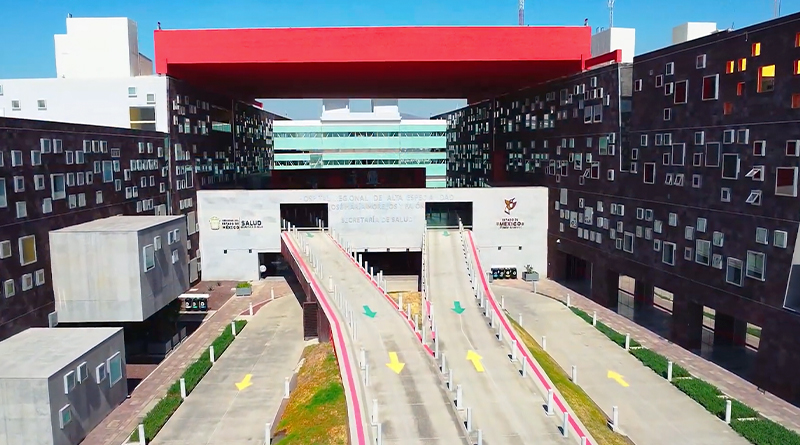 the facade of the Regional High Specialty Hospital of Zumpango, a modern architectural complex featuring wide access ramps and a distinctive design. The side walls are covered with numerous windows of varying sizes, while a large red structure stands out at the top, contrasting with the clear blue sky.