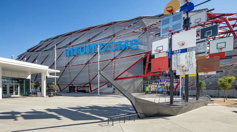 Exterior view of the Intuit Dome featuring its distinctive red and gray steel structure, with an artistic basketball backboard installation in front of the main entrance.