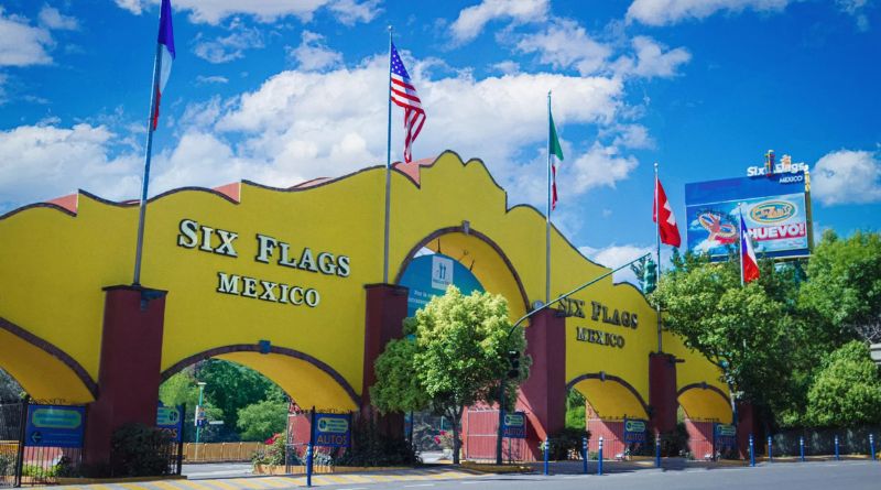 Main entrance of Six Flags Mexico featuring its iconic yellow arch, surrounded by international flags under a bright, inviting sky.